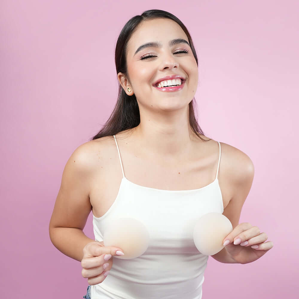 Uva Circular Nipple Covers Nude model smiling and holding nipple covers against a pink background.
