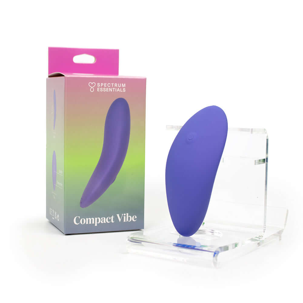 Spectrum Essentials Compact External Vibrator Purple in its packaging, showcasing a slim, ergonomic design for versatile play.