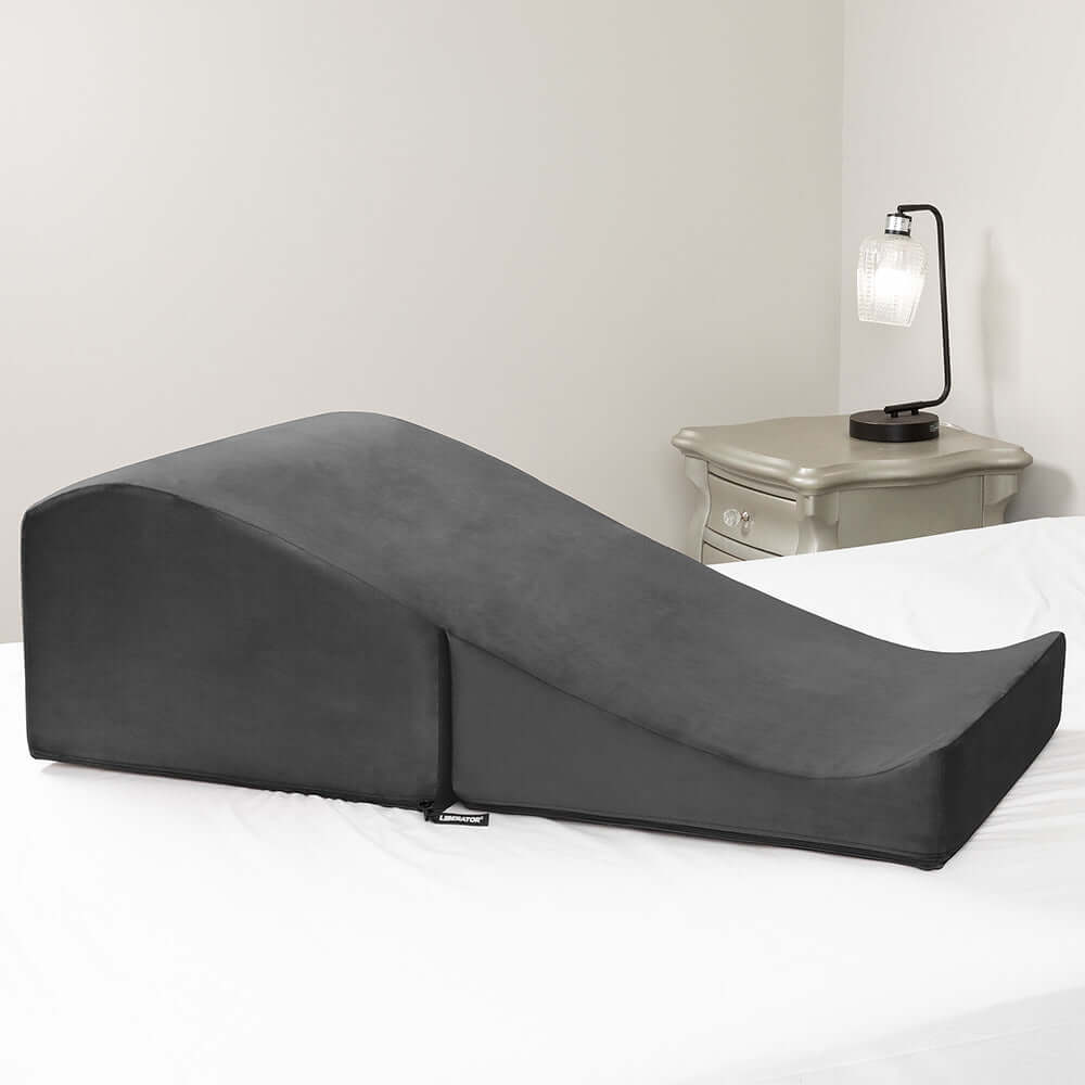 Liberator Flip Ramp With Slip Cover Lush Black positioned on a bed, offering ergonomic support and versatile use.