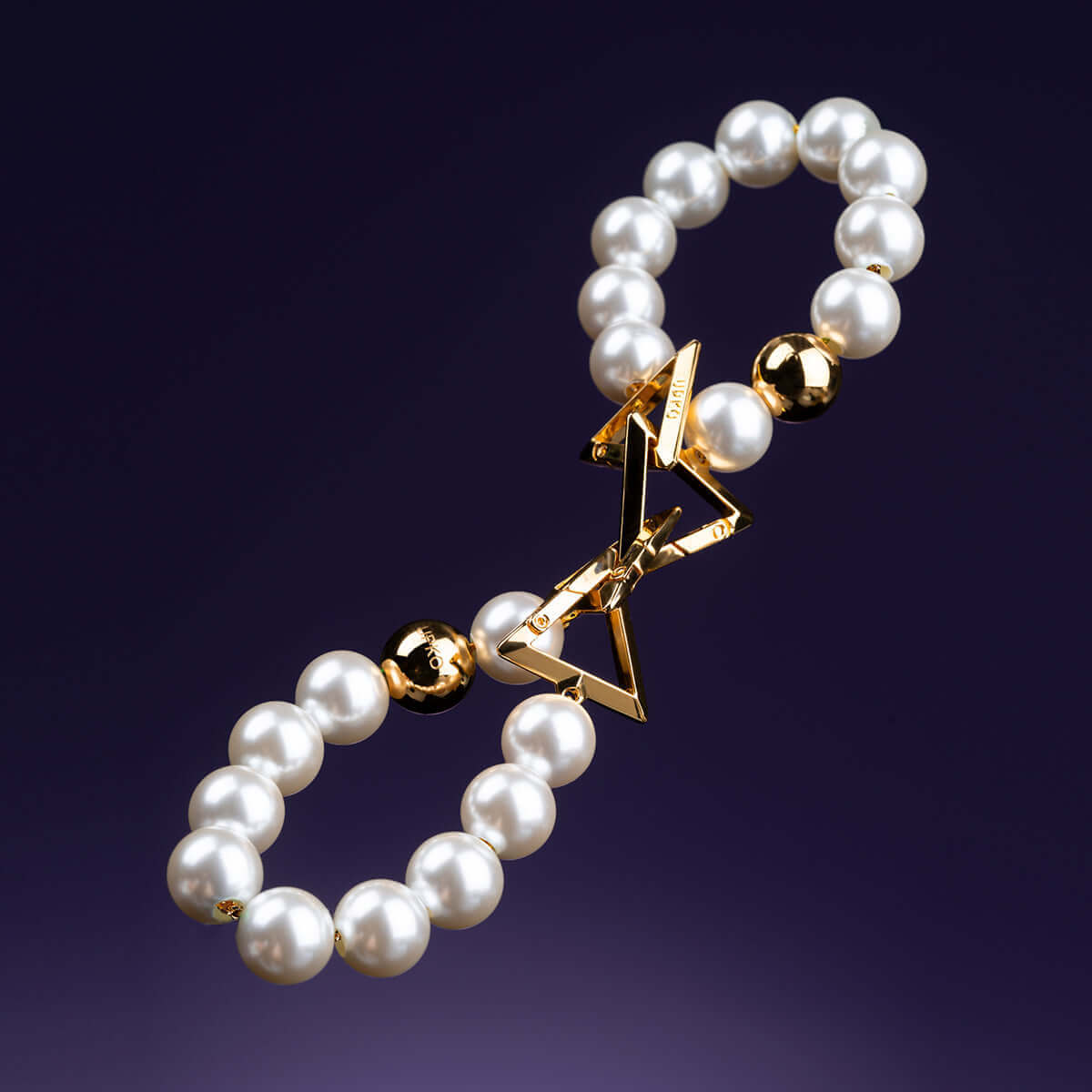 Elegant pearl bracelet handcuffs with gold accents on a dark background.