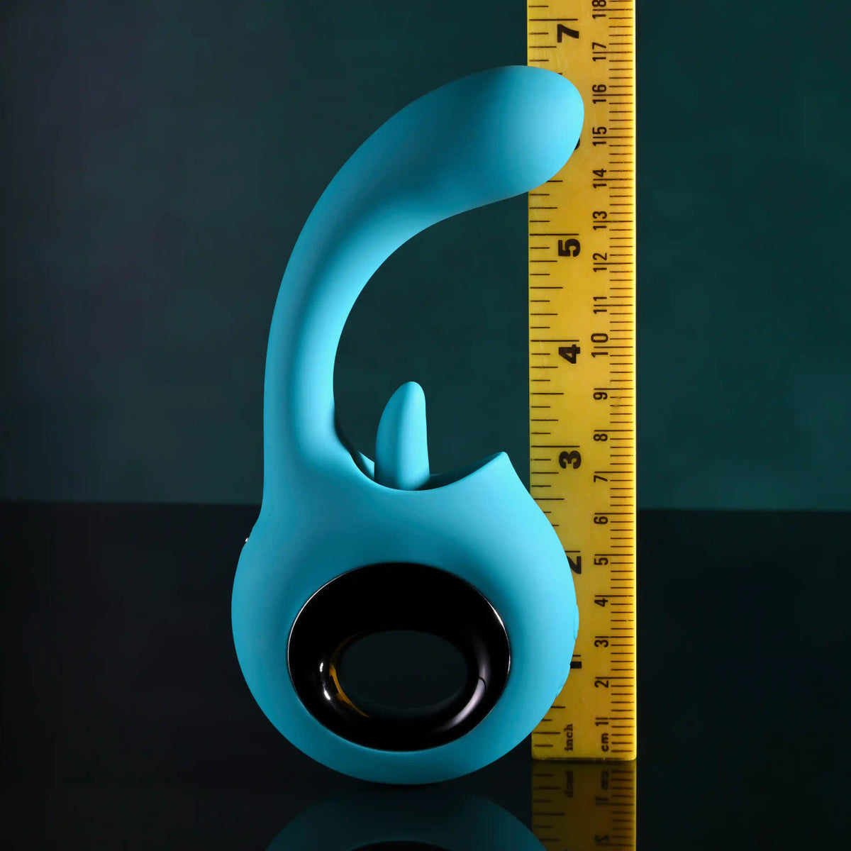 Evolved How Many Licks Silicone Vibrator Blue next to a ruler for size comparison on a dark background.