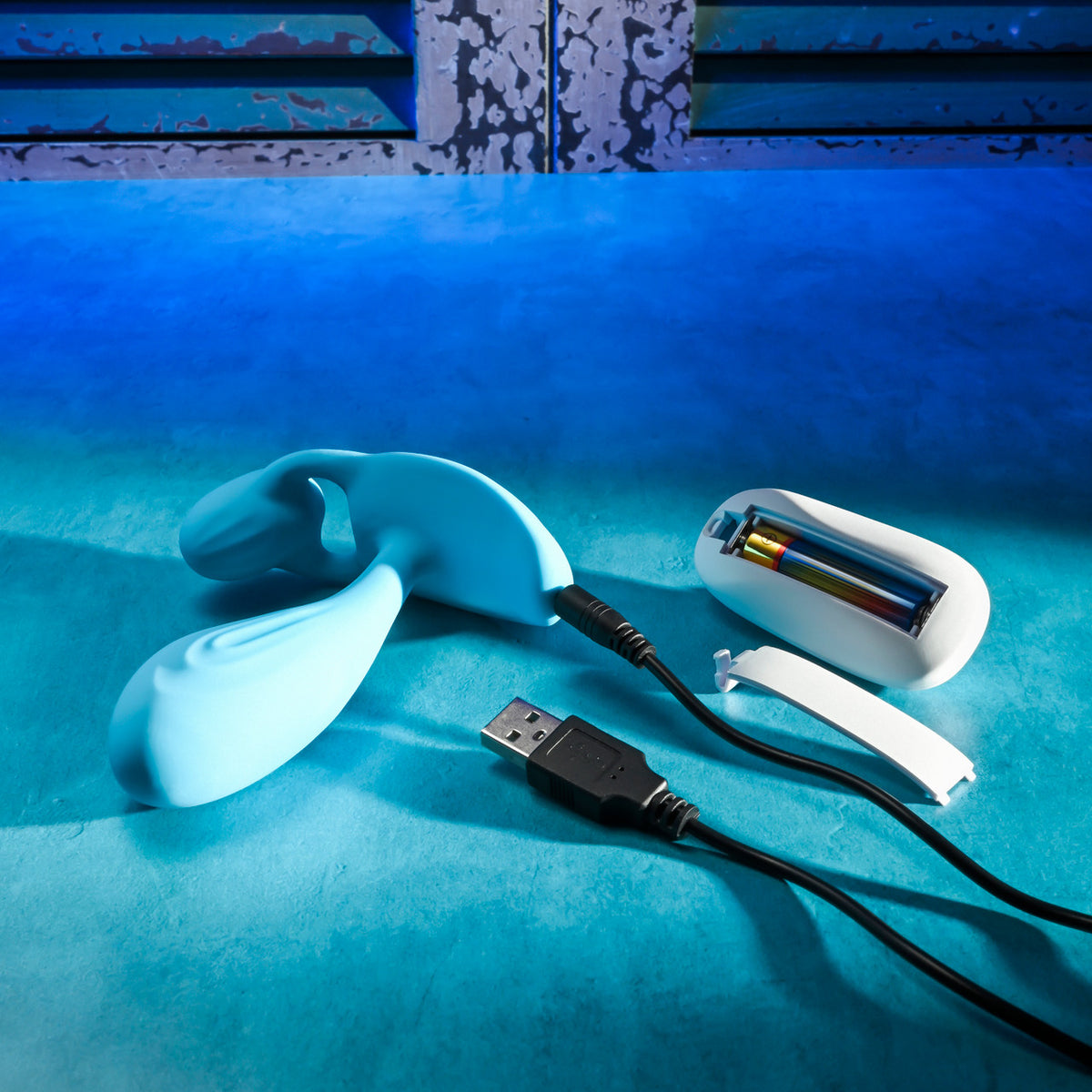 Gender X Wear Me Out Wearable Dual Vibrator Blue with charging cable and battery pack on a blue background.