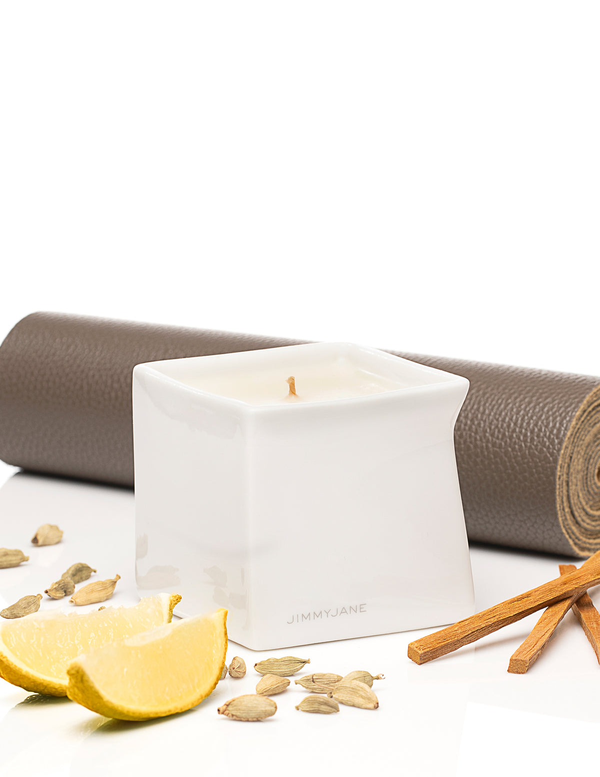 Jimmyjane Natural Massage Oil Candle 4.5 Oz Santal displayed with lemon and spices on a yoga mat.