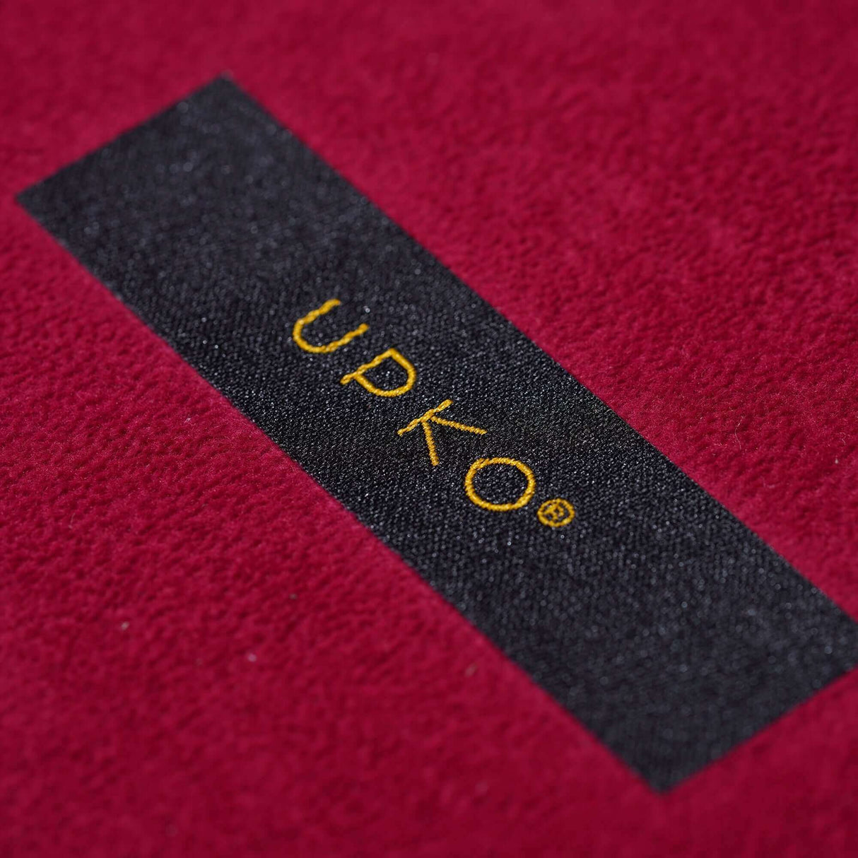 Close-up of UPKO logo on luxurious red fabric, showcasing quality craftsmanship of bondage tools set.