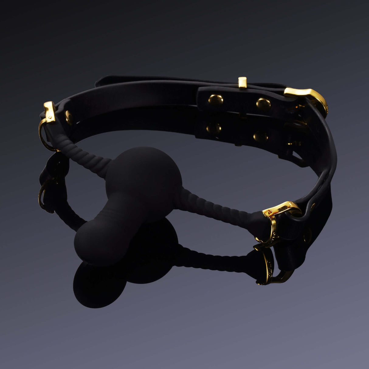 Black silicone dildo-shaped mouth gag with gold hardware accents on a black background.