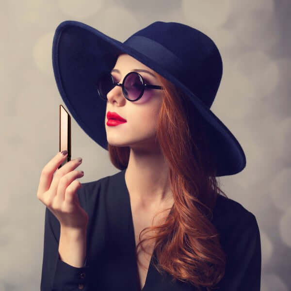 Woman wearing a large navy hat and sunglasses, holding a gold object, exuding elegance and style.