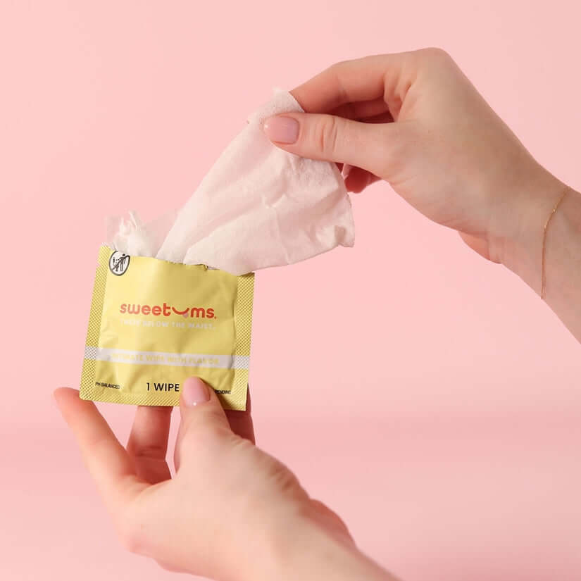 Person holding Sweetums Pina Colada Flavored Intimate Wipes packaging with a wipe partially pulled out.