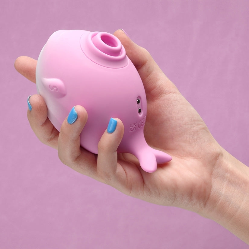 Hand holding Tracys Dog Whalo Air Suction Massager in pink against a soft background.