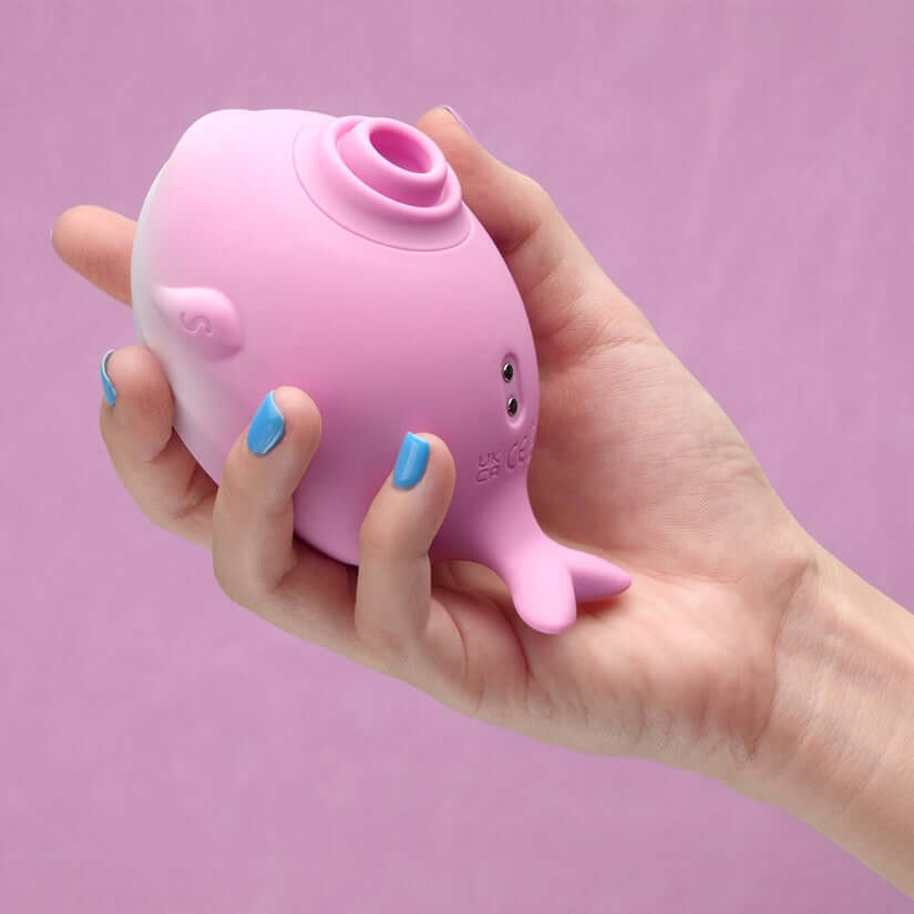 Hand holding Tracys Dog Whalo Air Suction Massager in pink against a soft background.
