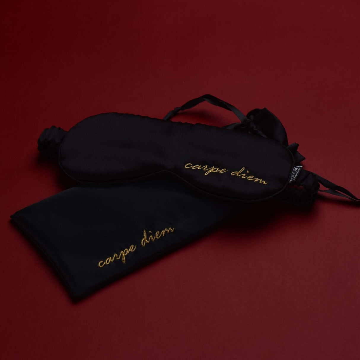 Carpe Diem premium silk blindfold and satin storage bag on a deep red background.