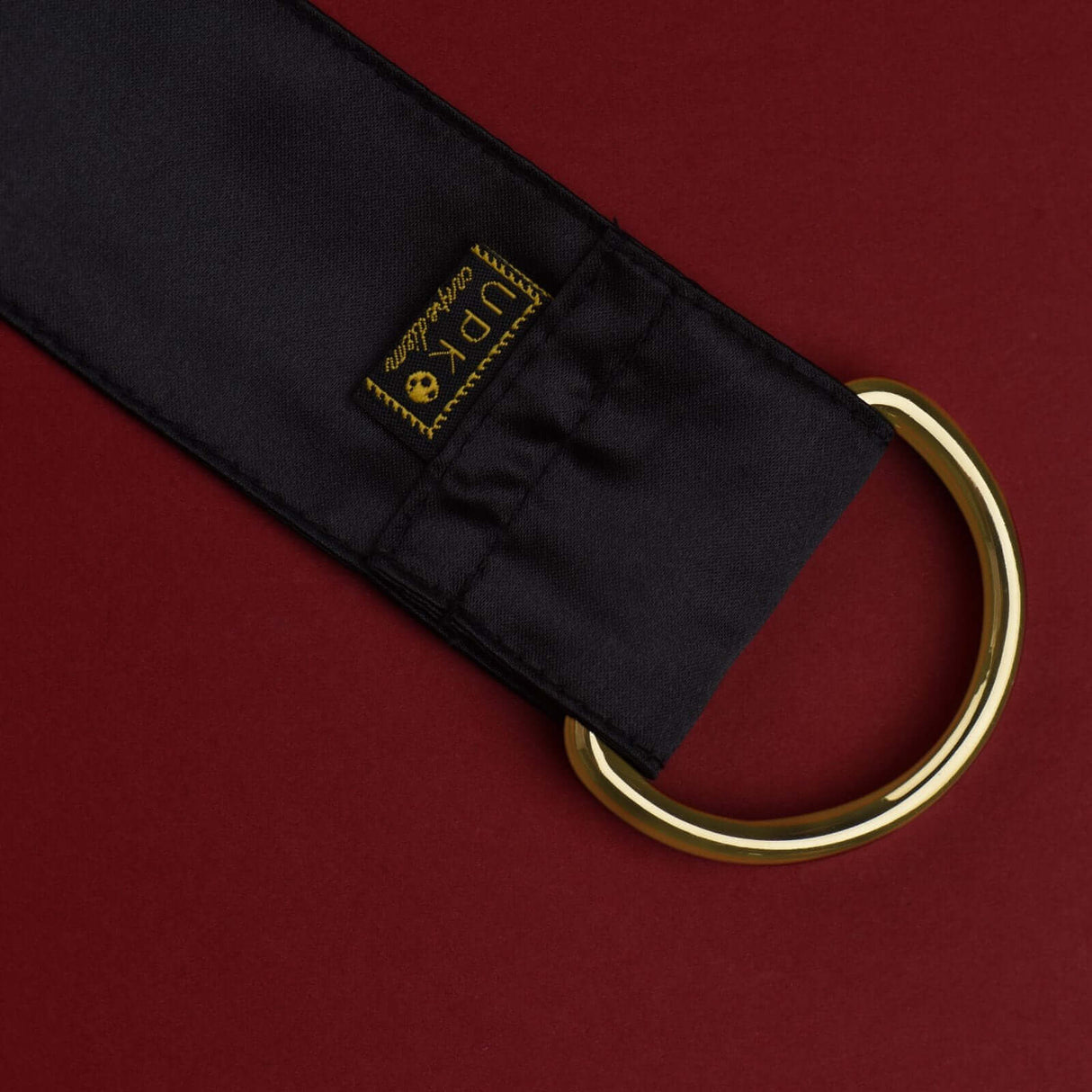 UPKO Carpe Diem silk strap with gold ring, perfect for bondage and restraint play. Premium quality design on red background.