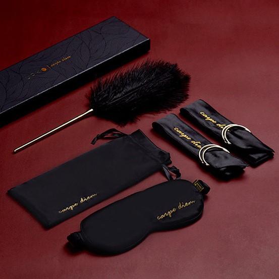 Carpe Diem Premium Silk Bondage Set featuring blindfold, satin ribbons, feather tickler, and storage bag on a red background.