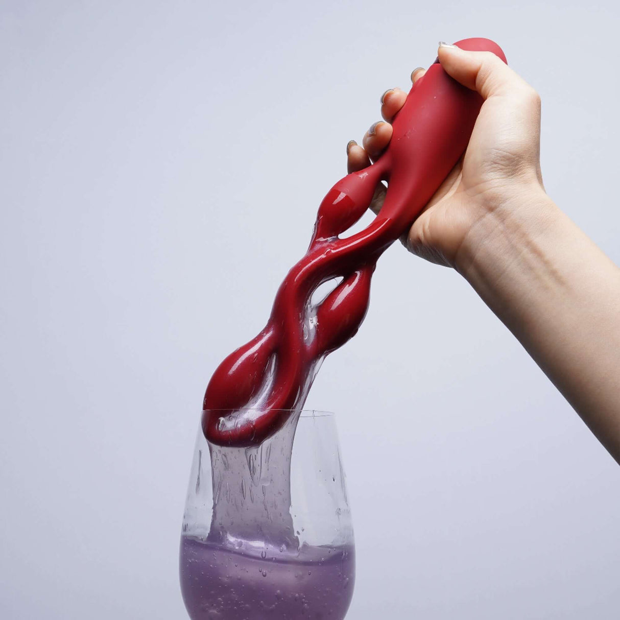 Red UEROS multi-motor pulse vibrator in hand demonstrating water resistance and unique design over a glass.