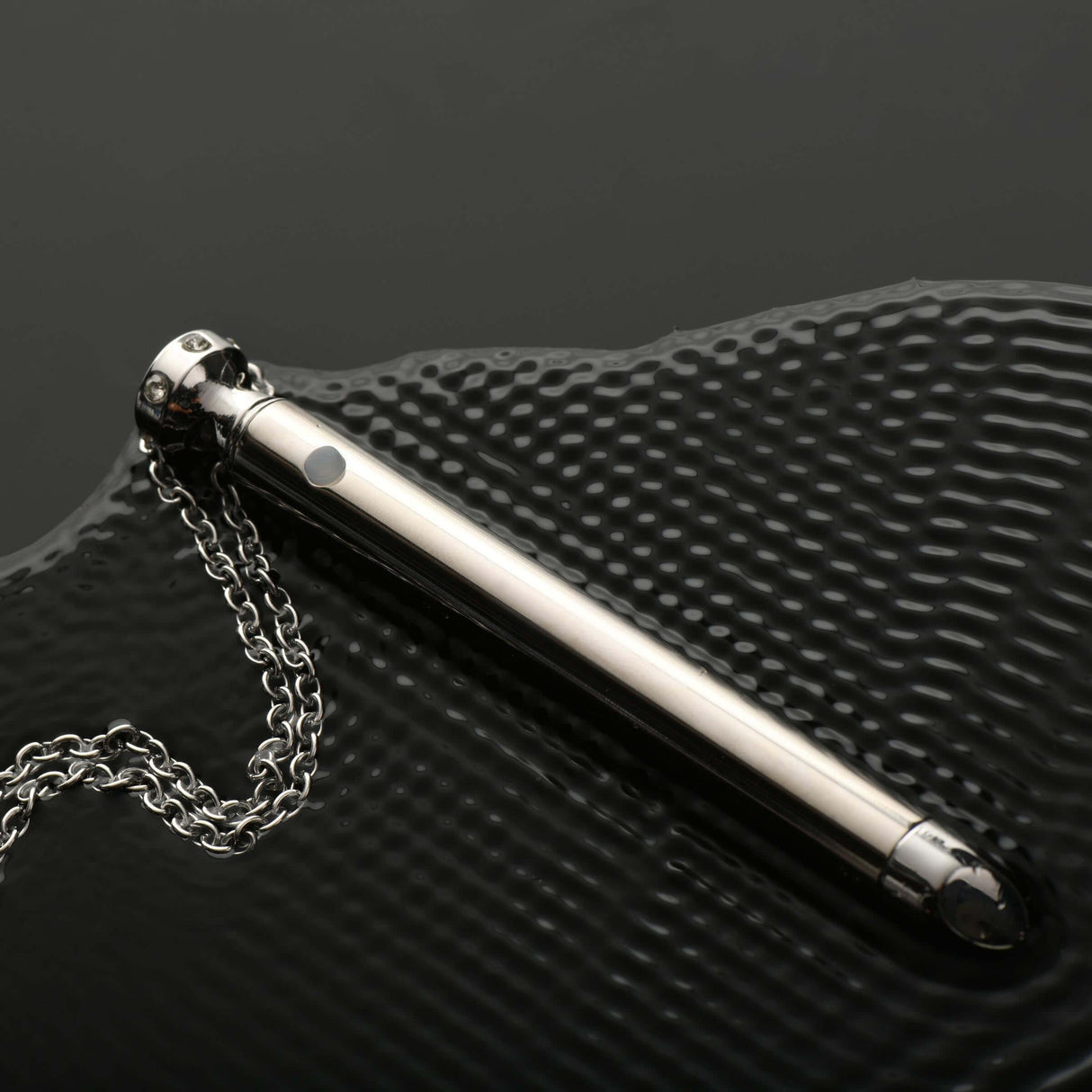 Charmed 7X Vibrating Necklace Silver on a textured surface showcasing its sleek design and chain.