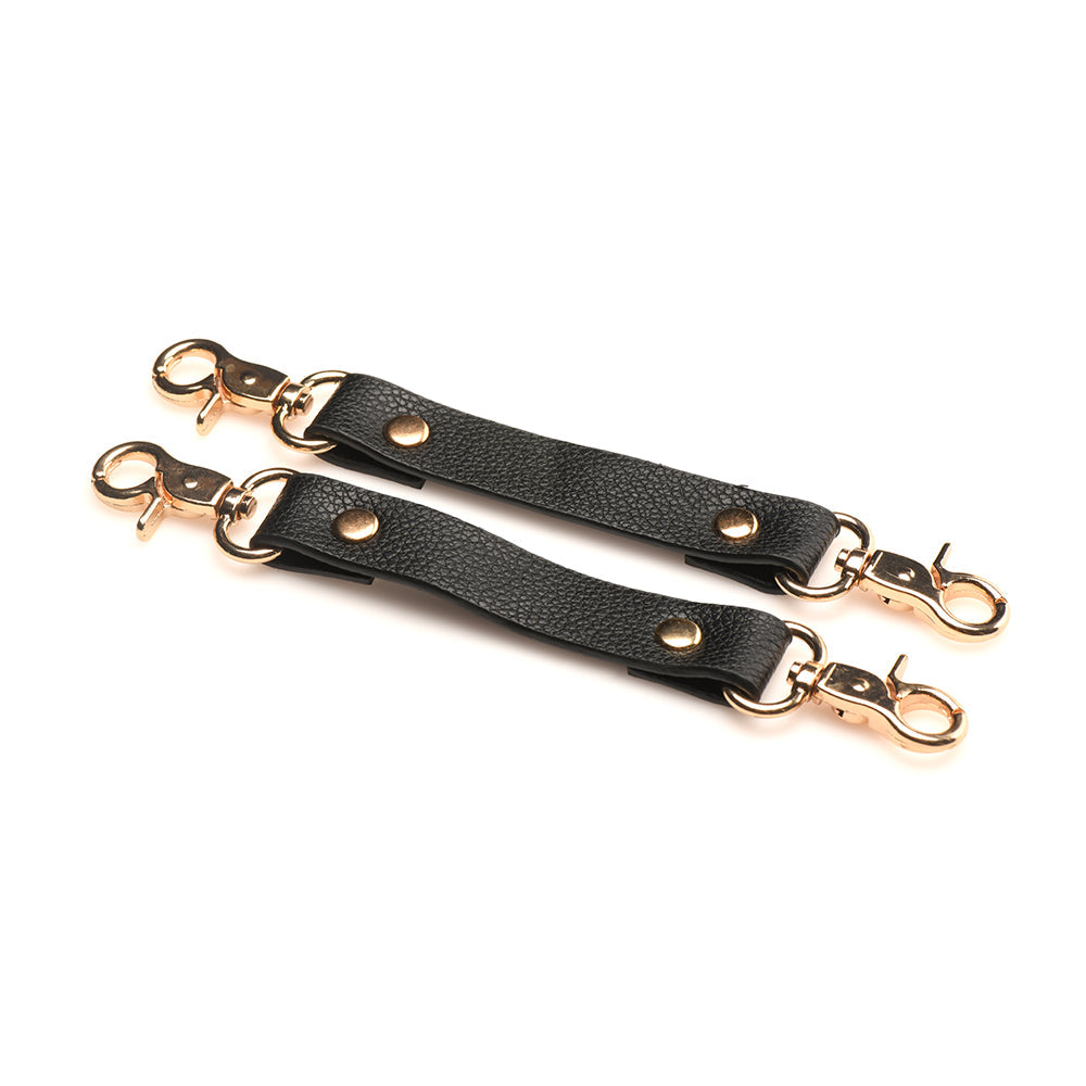 Black vegan leather cuff connectors with gold-tone clips for adjustable restraints.