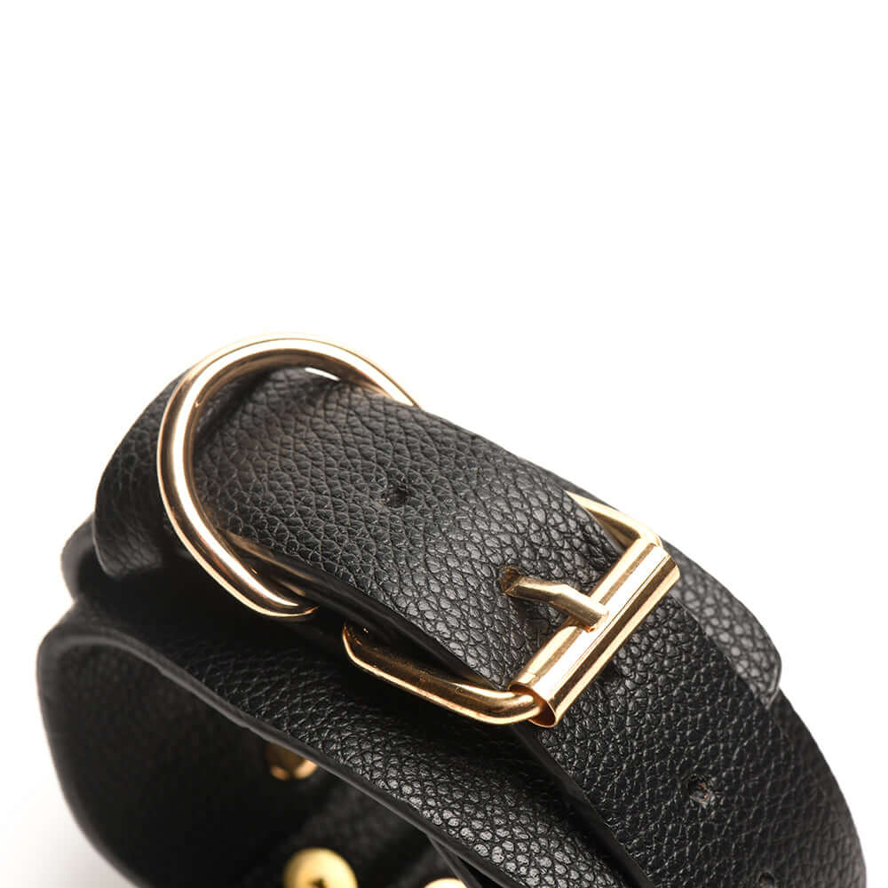 Close-up of a black vegan leather cuff with a gold buckle, part of the Bedroom Bliss Lover's Restraints Set.