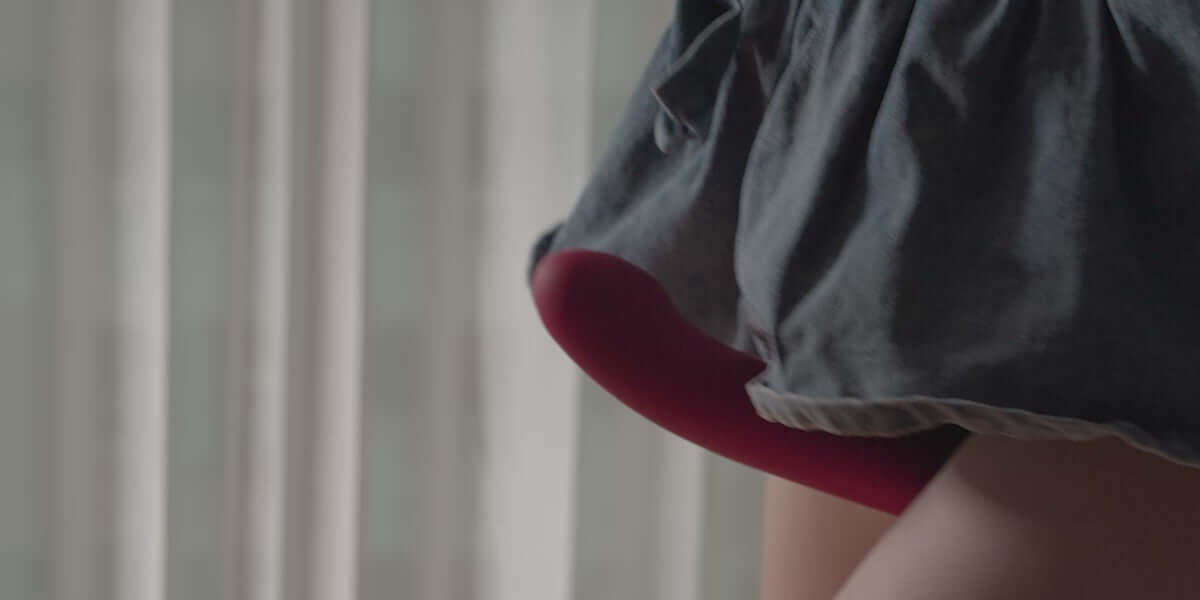 Lovense Strapless Harness for Lapis peeking from beneath a garment, showcasing its vibrant red design.