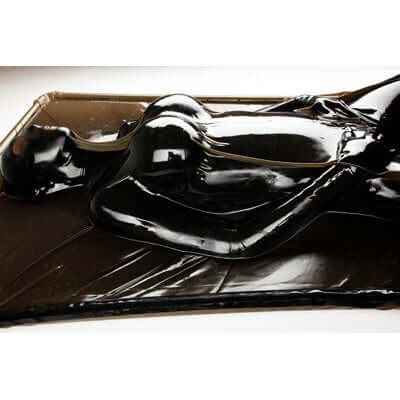 Extreme Black Latex Vacuum Bed with occupant tightly sealed in glossy black latex.