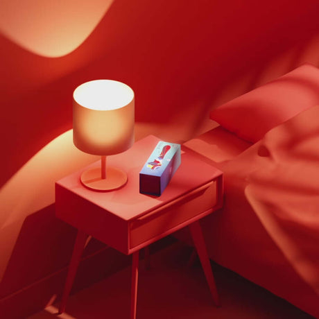 Biird Gii Glow Massager Mint displayed on a bedside table with a lamp in a vibrant red setting.