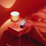 Biird Gii Glow Massager Lilac displayed on a bedside table next to a lamp in a cozy red room.
