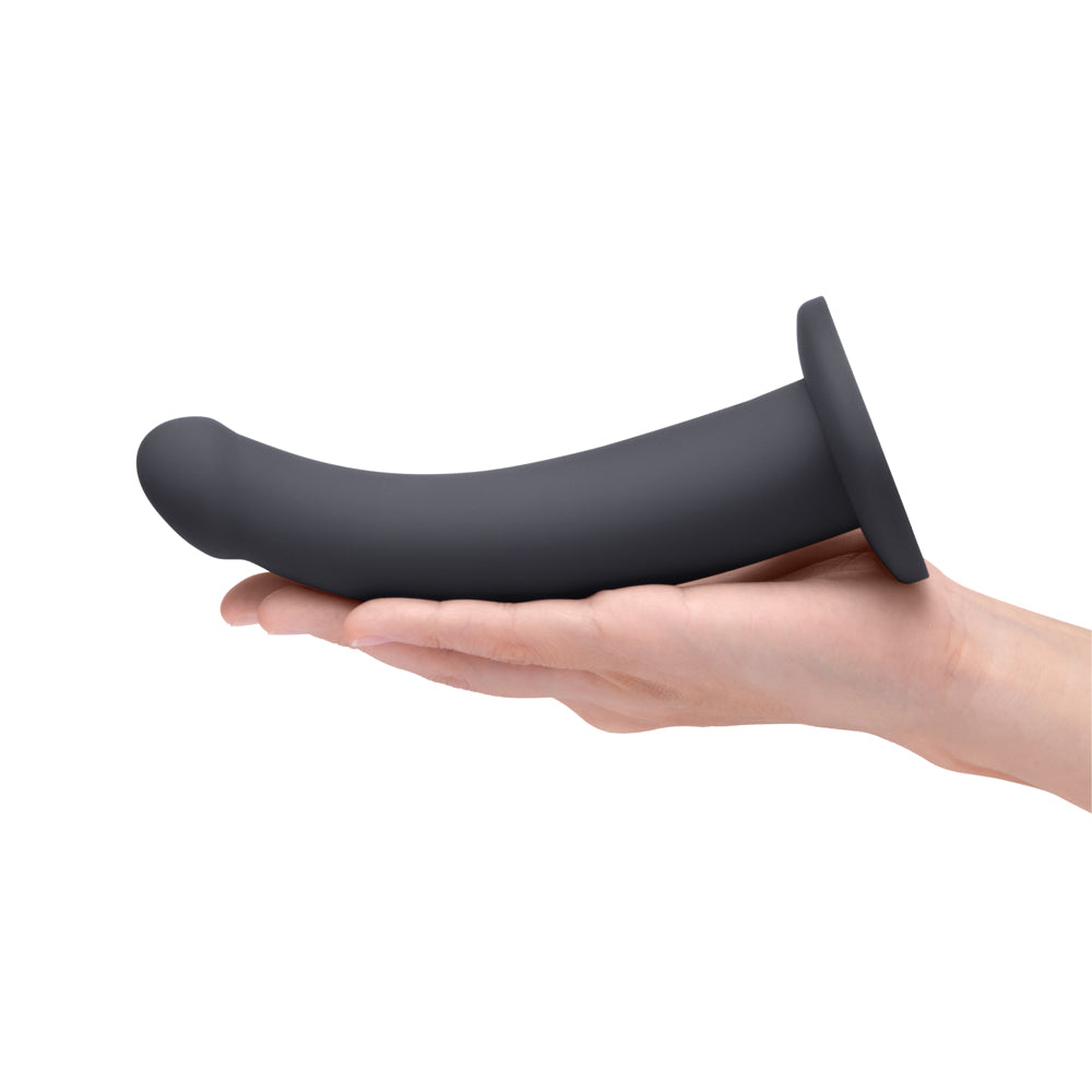 B-Vibe Essentials 7 Inch Smooth Silicone Dildo Black held in a hand, showcasing its sleek design and smooth finish.