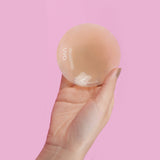 UVA Caramel Non-Adhesive Round Nipple Covers held in hand against a pink background.