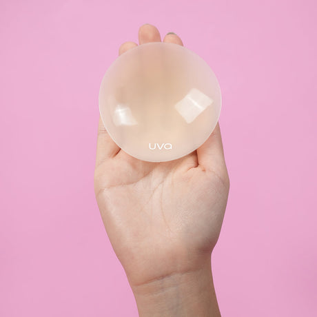 UVA Vanilla Non-Adhesive Round Nipple Covers held in hand against a pink background.