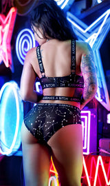 Karma's a Bitch Bralette and Cutout Panty Set Black M L worn by model with neon lights in background.