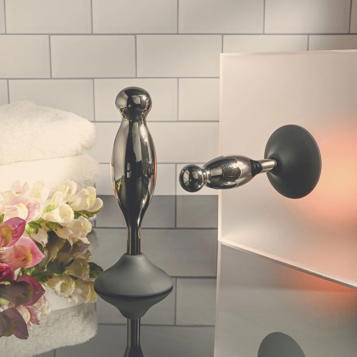 Evolved Joy Sticks 2 Piece Anal Plug Set Black Chrome displayed on a sleek surface with towels and flowers.