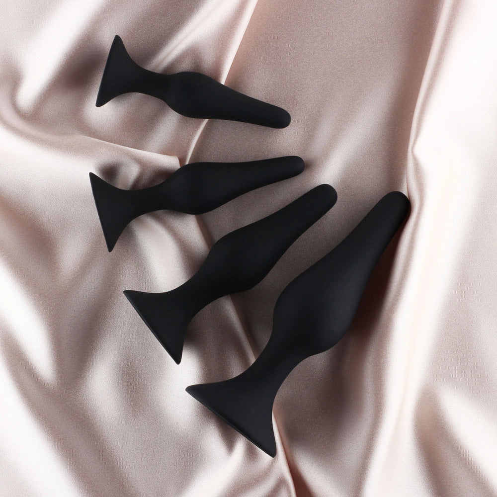 Edonista Alessandra 4 Piece Silicone Anal Plug Set Black displayed on soft satin fabric.