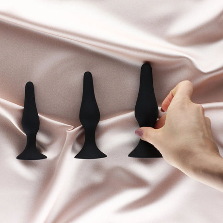 Edonista Alessandra 4 Piece Silicone Anal Plug Set Black displayed on silk, showcasing gradual sizes and user engagement.