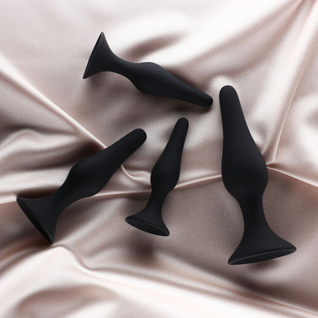 Edonista Alessandra 4 Piece Silicone Anal Plug Set Black displayed on a satin surface, featuring various sizes for comfortable use.
