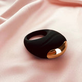 Edonista Luca Vibrating Penis Ring Black on soft pink fabric, featuring sleek design and gold accents.