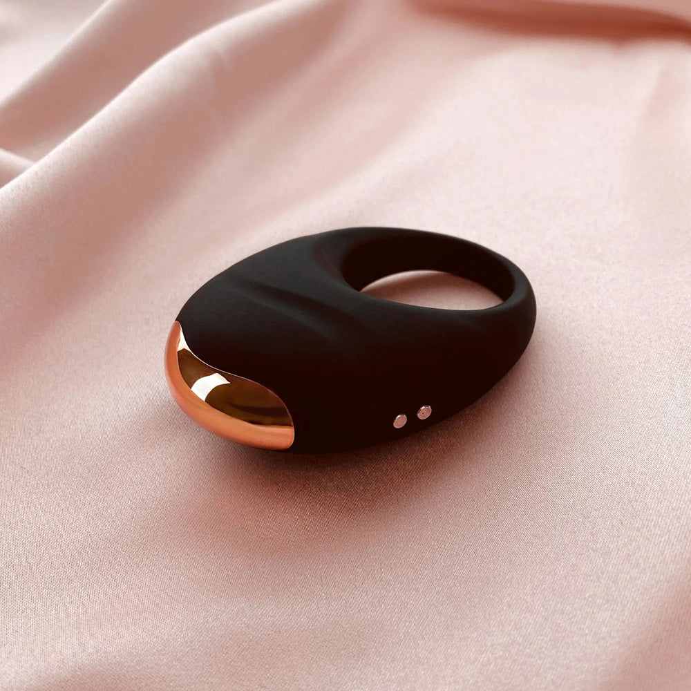 Edonista Luca Vibrating Penis Ring Black on soft pink fabric background, showcasing sleek design and luxurious finish.