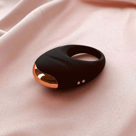 Edonista Luca Vibrating Penis Ring Black on soft pink fabric background, showcasing sleek design and luxurious finish.