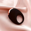 Edonista Luca Vibrating Penis Ring Black on soft satin fabric, showcasing its sleek design and comfortable fit.