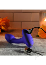 Gender X Anybody's Plug Silicone Vibrating Butt Plug Blue charging with a USB cable on a textured surface.