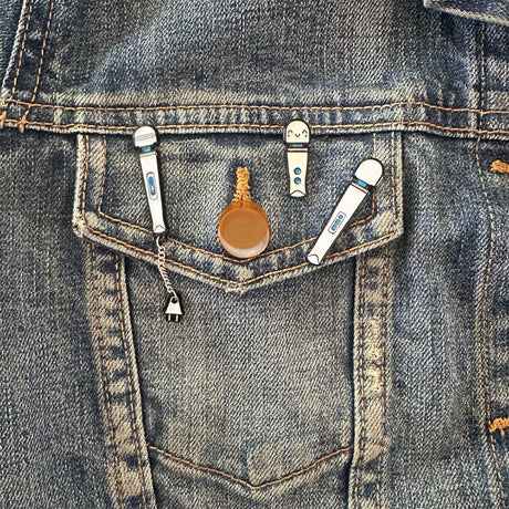 Wood Rocket Magic Wand Rechargeable Enamel Pin displayed on a denim jacket pocket.