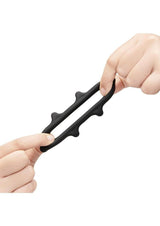 B-Vibe Flex Ring Spike Silicone Cock Ring Black showcased being stretched between two hands.