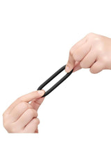 B-Vibe Snug Ring Lite Silicone Cock Ring 3 Pack Black being held and stretched by hands.