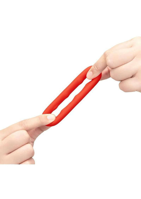 B-Vibe Flex Ring Grip Silicone Cock Ring Red being stretched between two hands, showcasing its flexibility and durability.