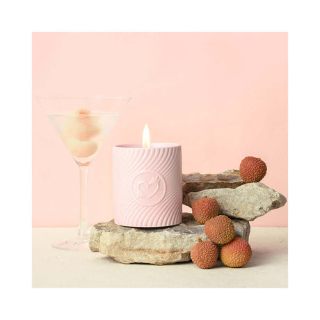 HighOnLove Pink Massage Candle Litchi Martini on stones with a cocktail and lychee fruit, enhancing romantic ambiance.