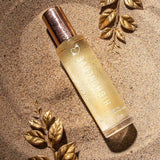 HighOnLove Dry Body Oil Spray bottle displayed on sand with golden leaves.