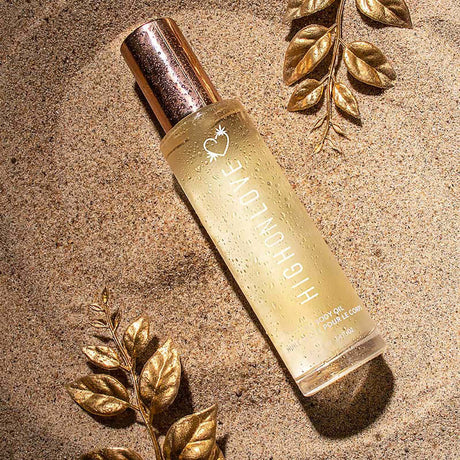 HighOnLove Dry Body Oil Spray bottle displayed on sand with golden leaves.