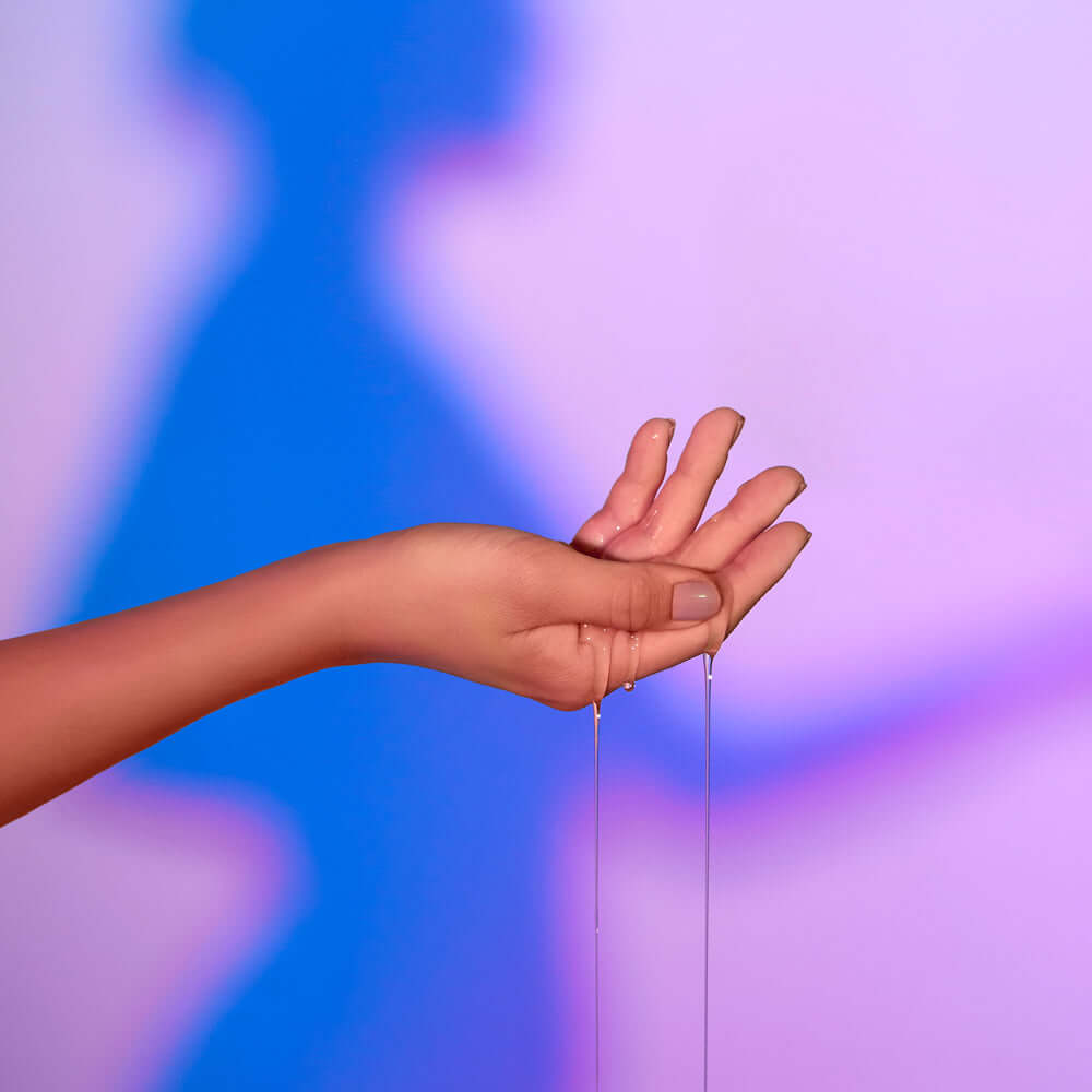 Love Me Tender Luscious & Heating Massage Oil Mojito 3.3 Oz pouring from a hand with colorful background.