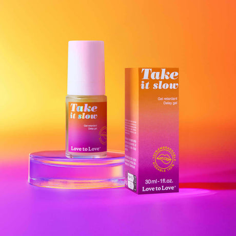 Love to Love Take It Slow Delay Gel 1 Oz with colorful packaging on a glass stand against a gradient background.