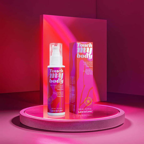 Touch My Body 2-in-1 Massage Fluid & Intimate Lubricant Ylang-Ylang 3.3 Oz displayed on a neon pink shelf.
