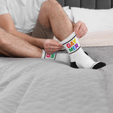 Man sitting on bed putting on Prowler Gaymer Socks with rainbow lettering.