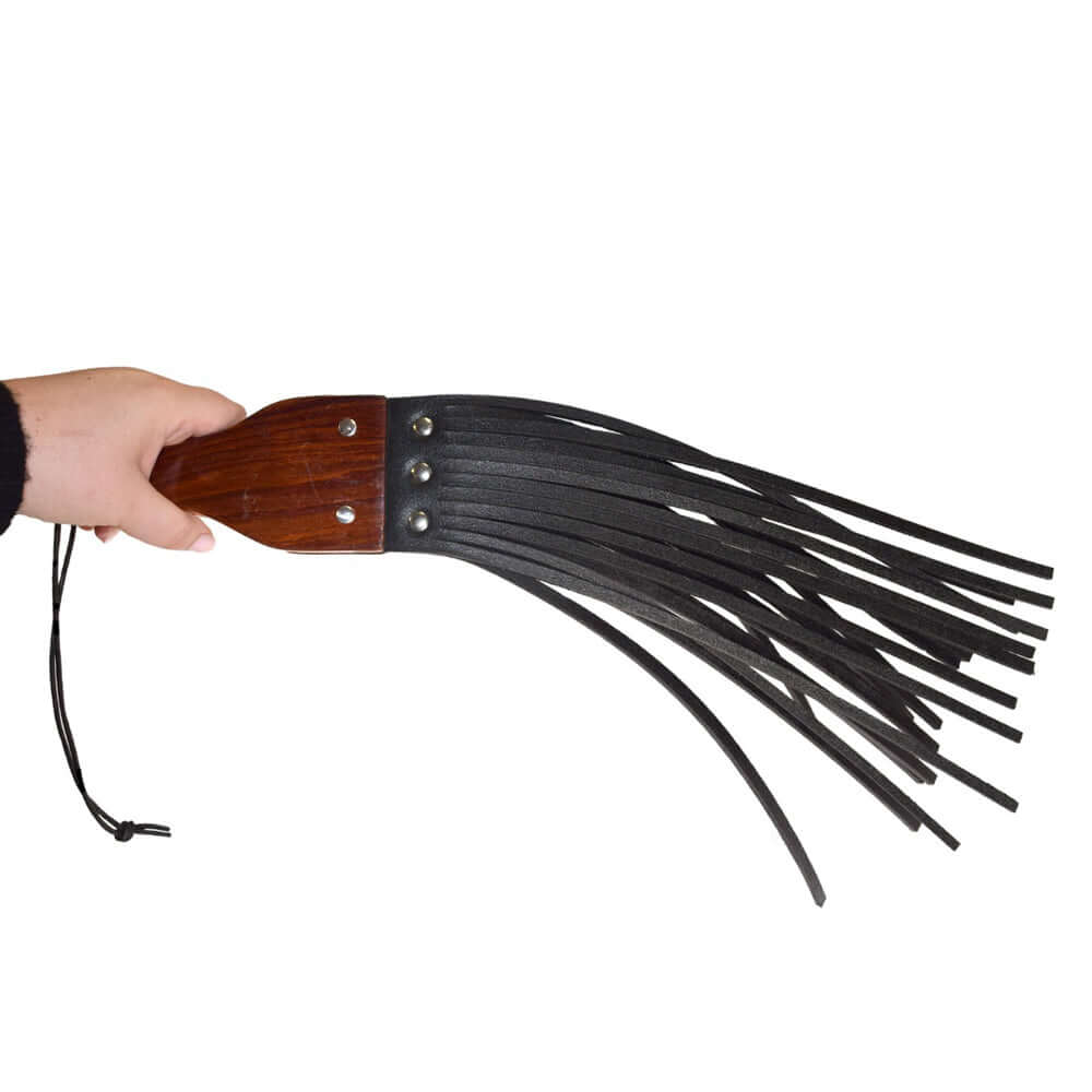 Prowler RED Leather & Wood Fringe Paddle in hand, showcasing durable leather and wooden handle with fringe details.