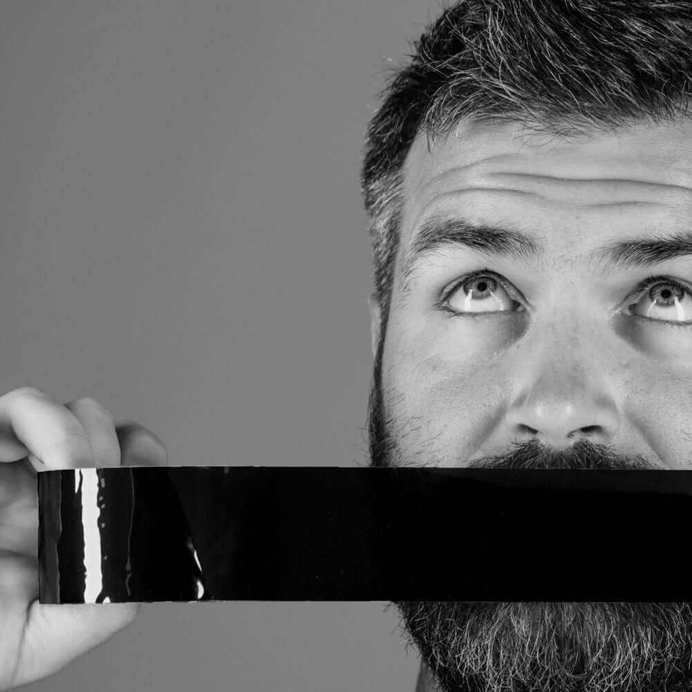 Man demonstrating Prowler Bondage Tape Restraints Black 20 m, showcasing its adhesive self-stick feature.